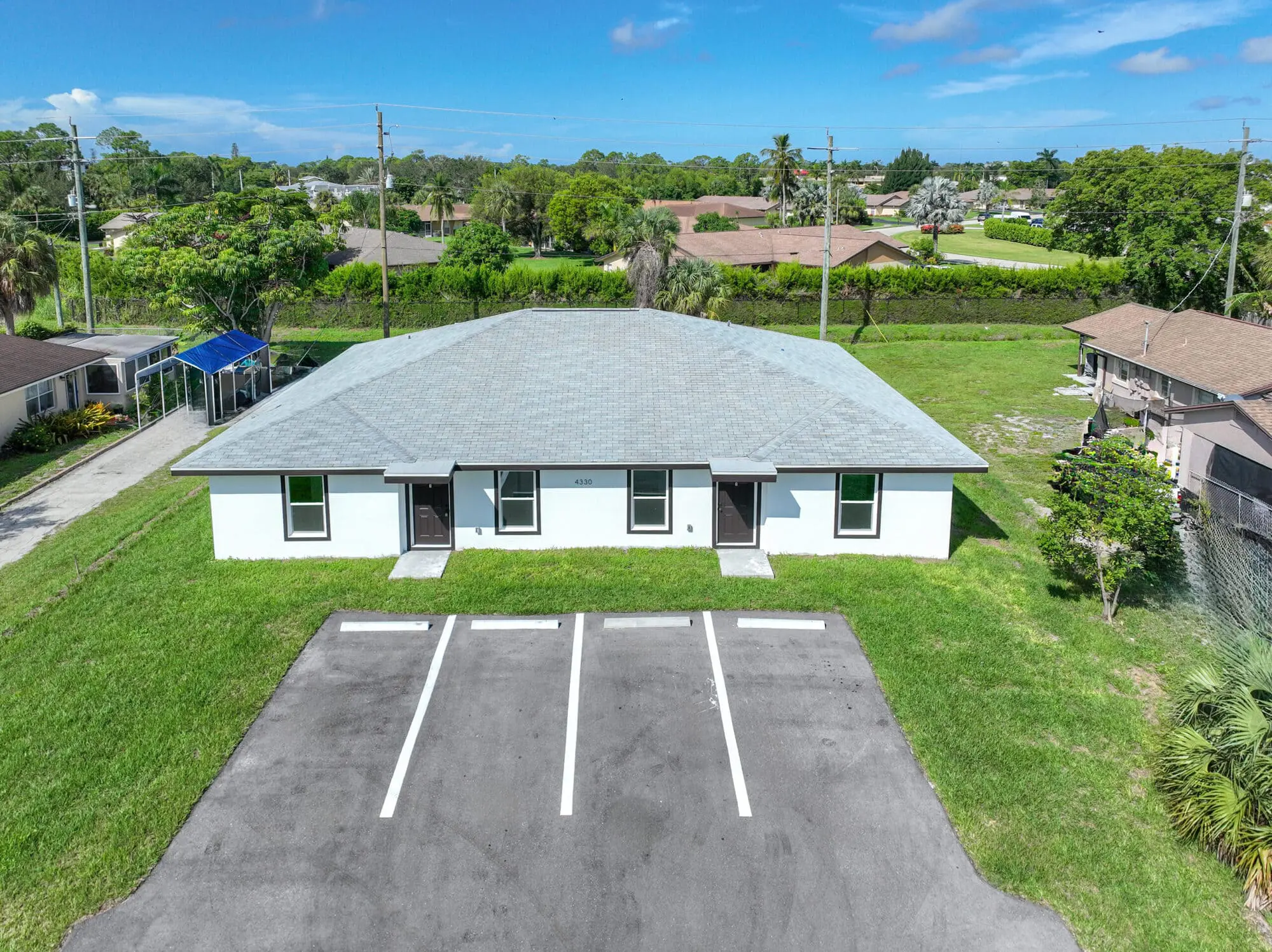 Aerial view of a white duplex by TN Capital Investments in Naples, FL, with gray roof, parking, and green lawn on Gulfstream Dr.