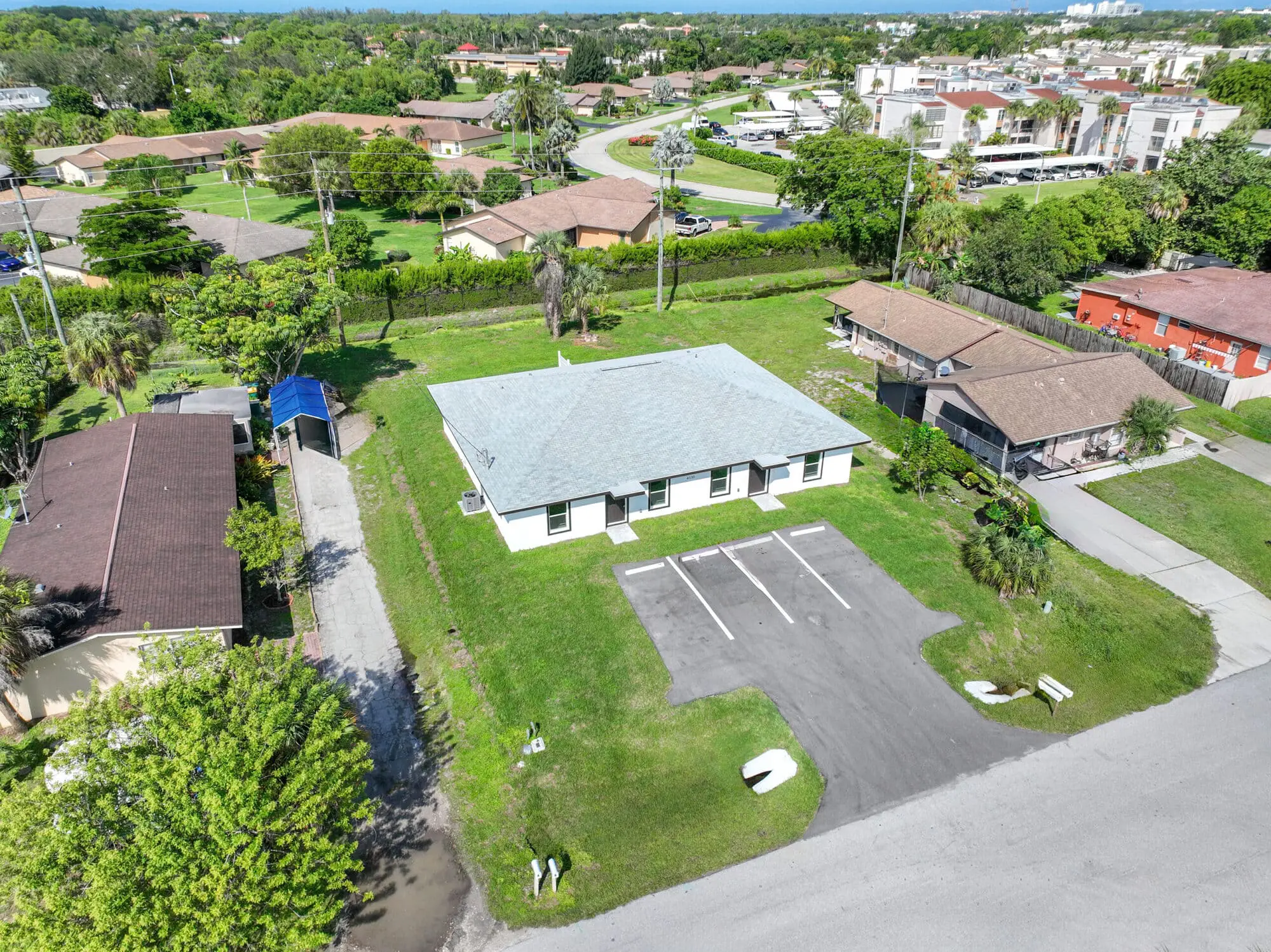 Aerial view of TN Capital Investments in Naples, FL—a single-story white building with gray roof, parking lot, and green lawn.