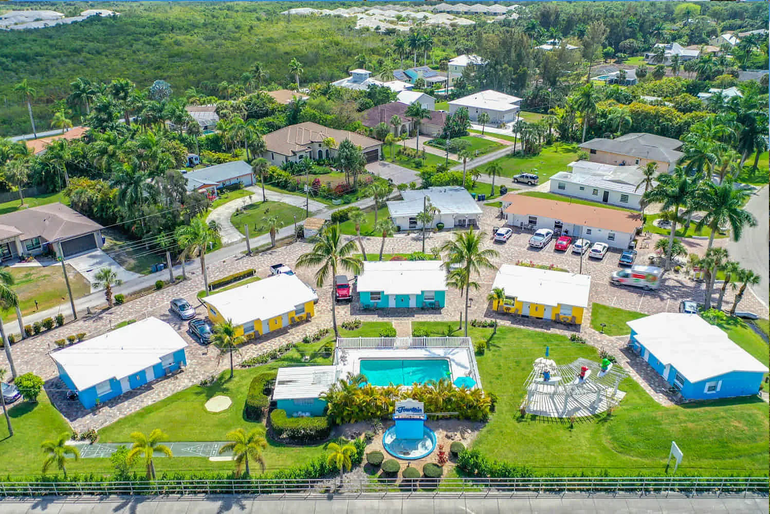 Aerial view of a TN Capital Investments resort in Naples, FL with colorful cottages, central pool, palm trees, and green space.