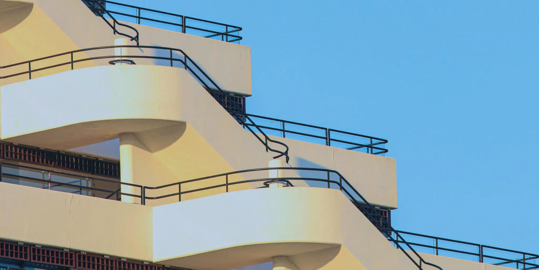 A sleek building with curved balconies and black railings, by TN Capital Investments in Naples, FL, set against a blue sky.