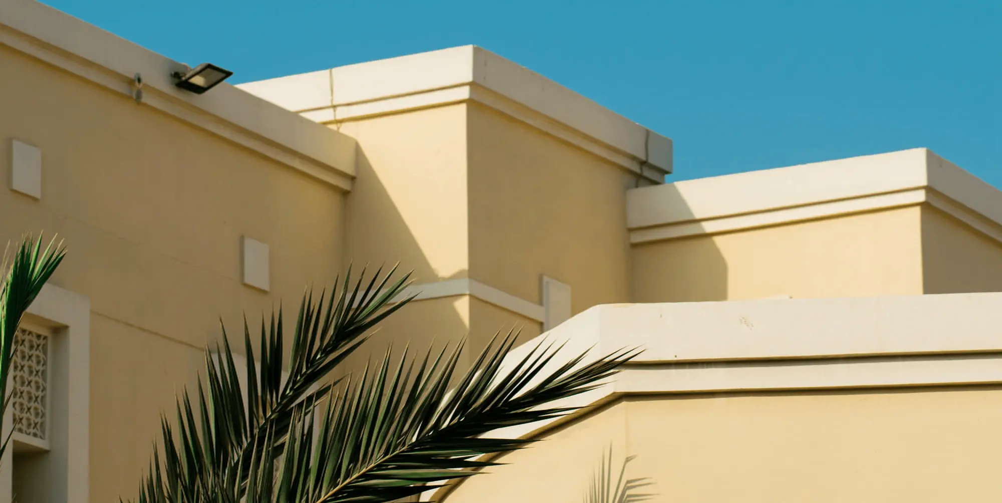A beige Living Building with white trim and sharp rooftops, palm branch, and blue sky, for TN Capital Investments in Naples, FL.