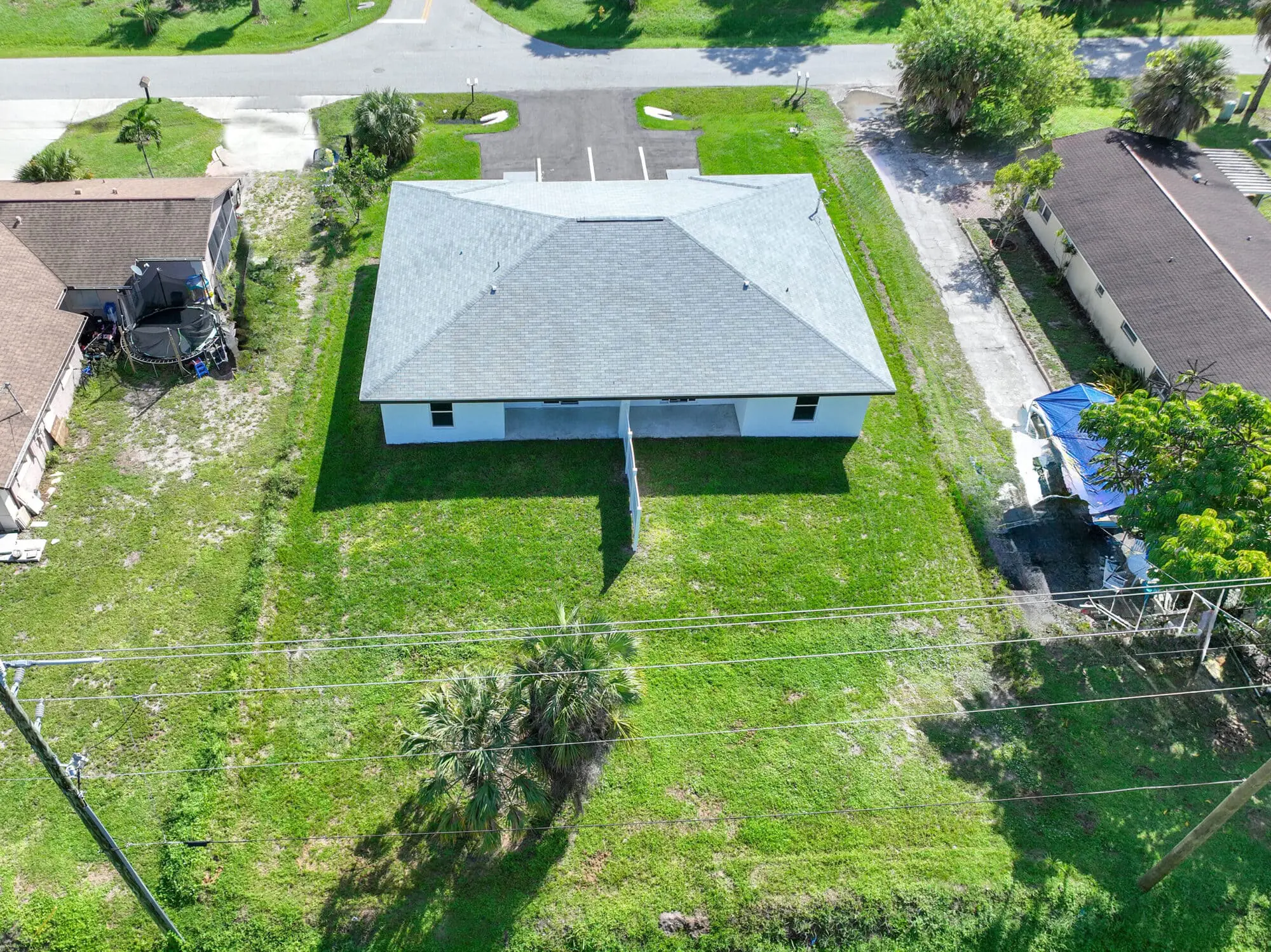 Aerial view of TN Capital Investments' single-story white building with gray roof in Naples, FL, beside other buildings and a lot.