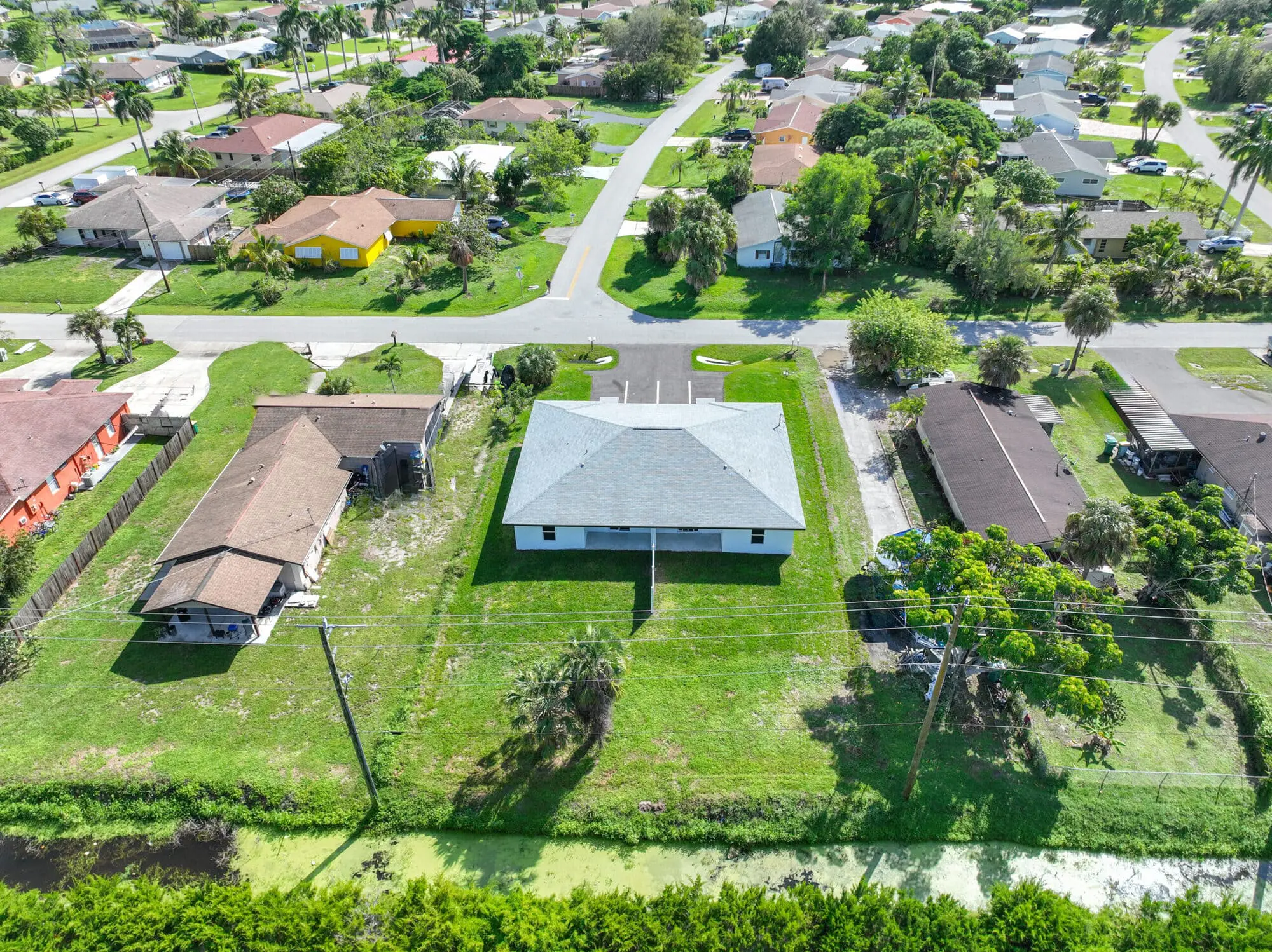 Suburban neighborhood in Naples, FL, along Gulfstream Drive with TN Capital Investments, tree-lined streets, lawns, and canal.