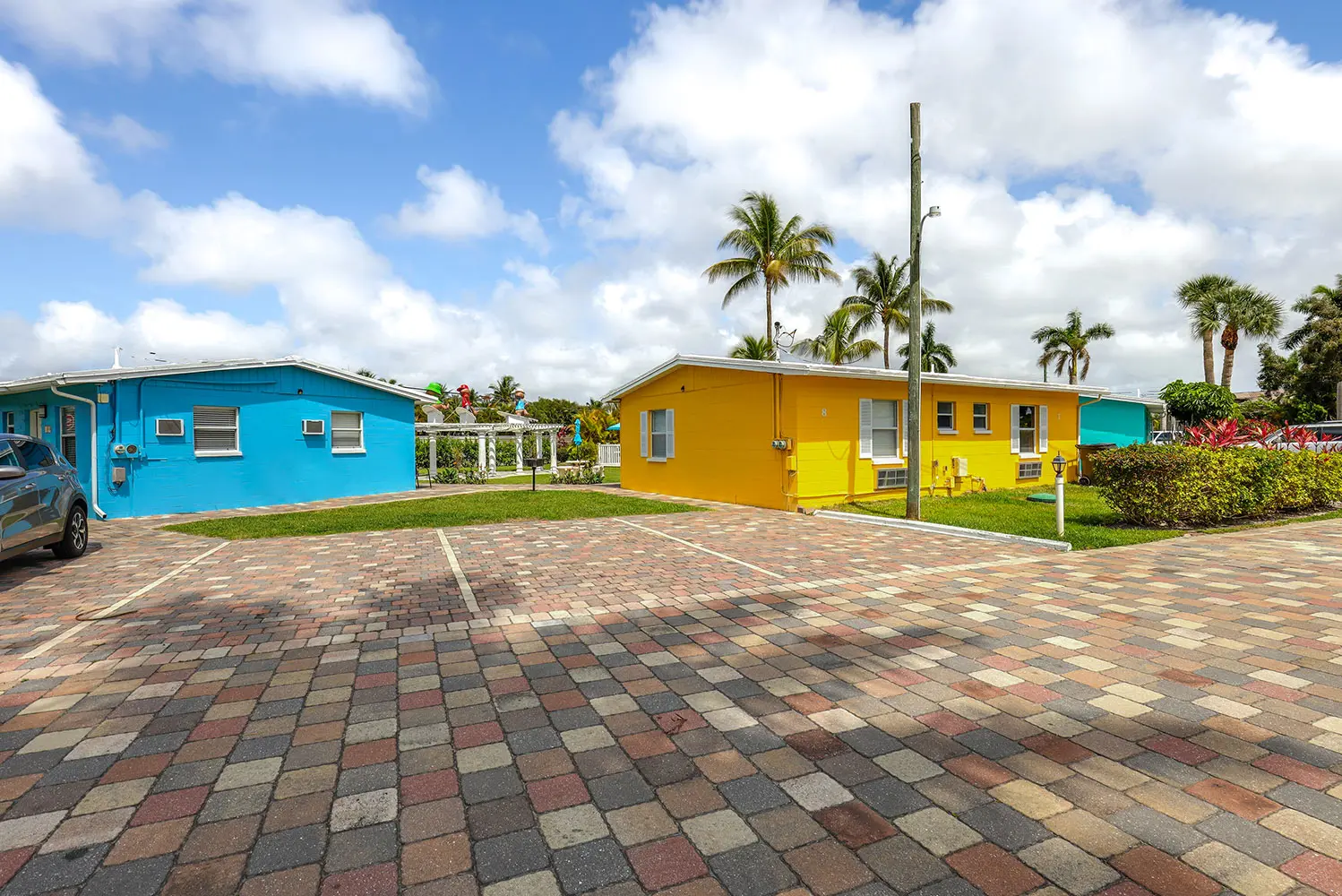 Blue and yellow single-story homes by TN Capital Investments in Naples, FL, with palm trees and an empty parking area nearby.