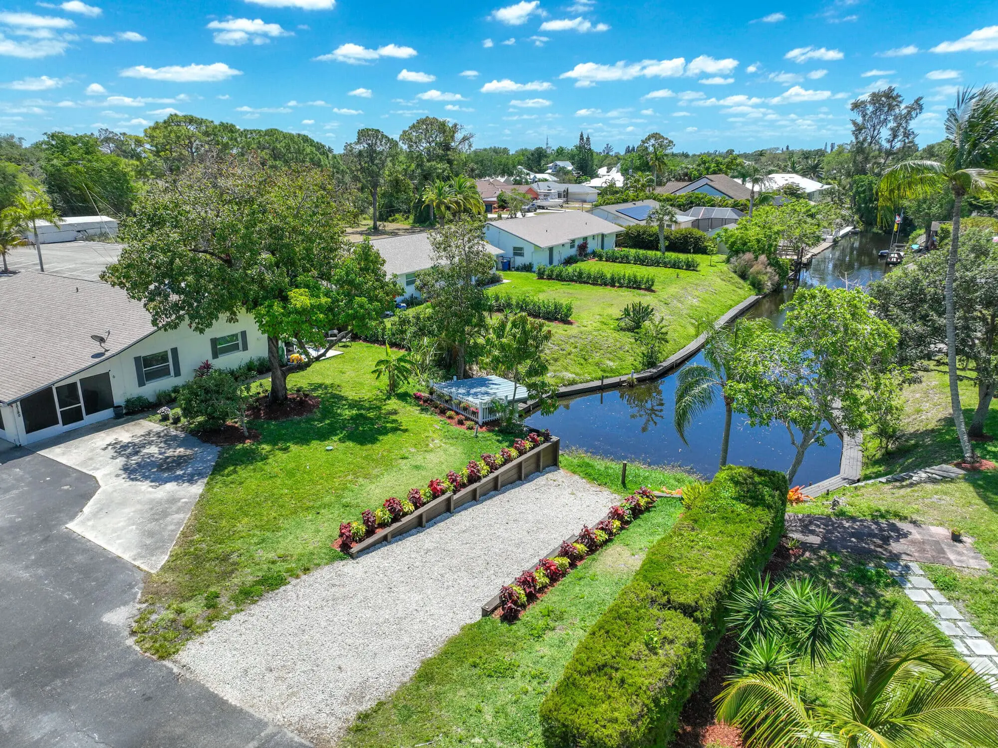 Suburban home with driveway, landscaped yard, and canal, managed by TN Capital Investments in Naples, FL under a blue sky.