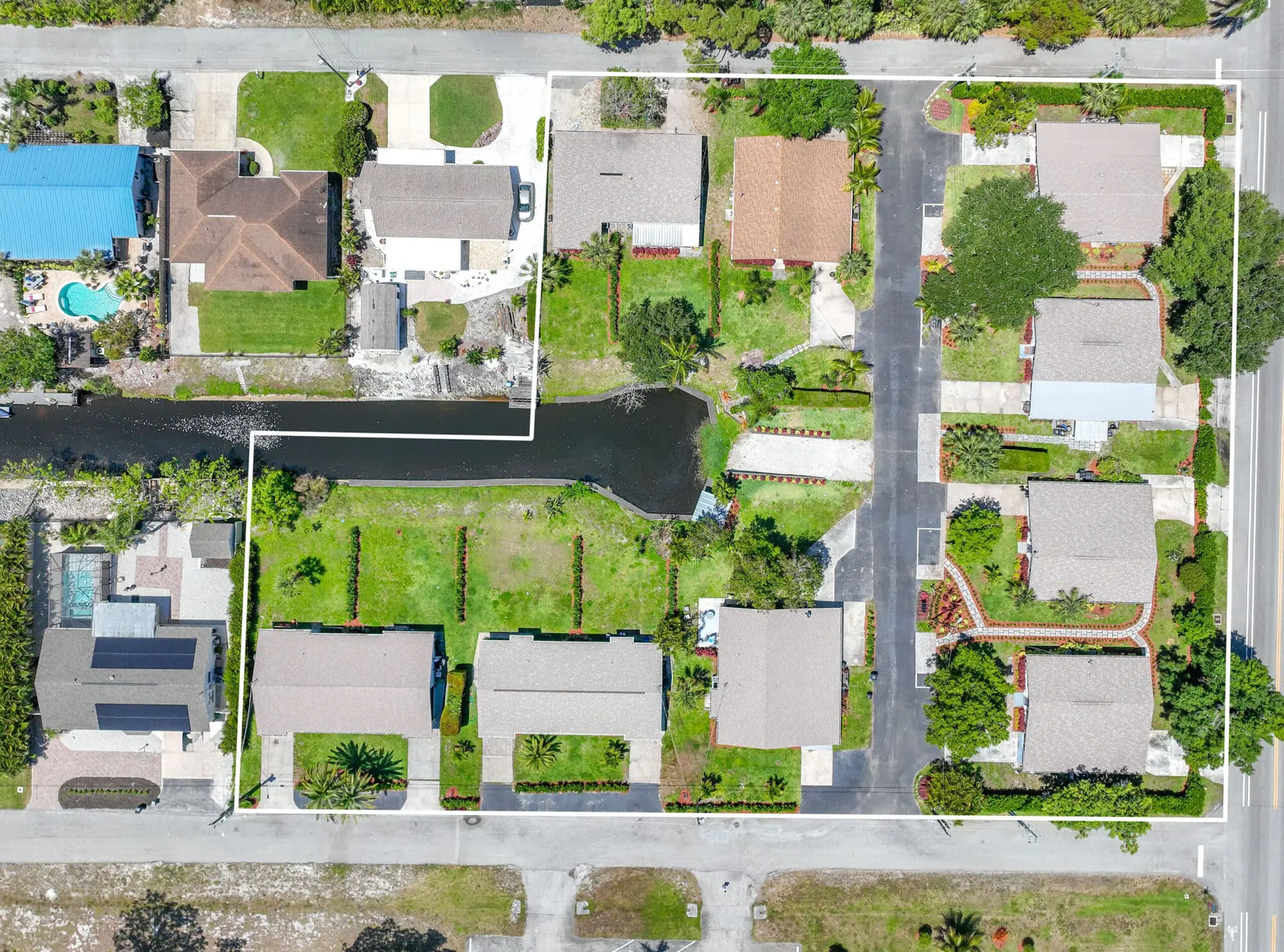 Aerial view of a Naples, FL neighborhood with houses, yards, driveways, canal, and TN Capital Investments property boundaries outlined.