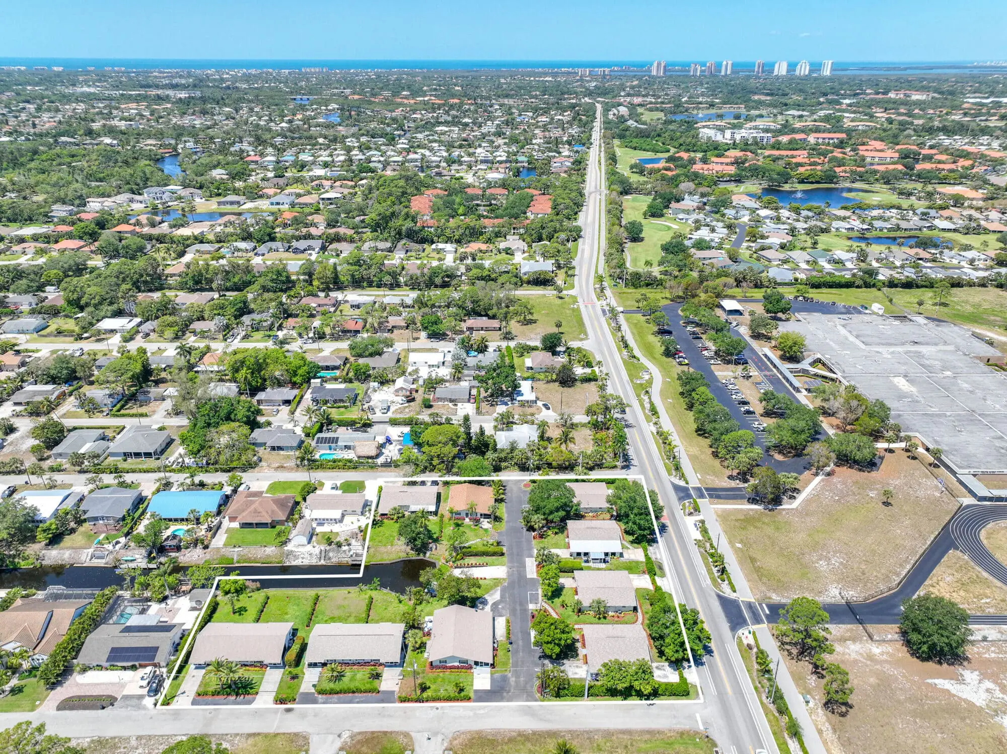 Suburban neighborhood in Naples, FL with houses, trees, and roads near the coast; TN Capital Investments visible in the distance.