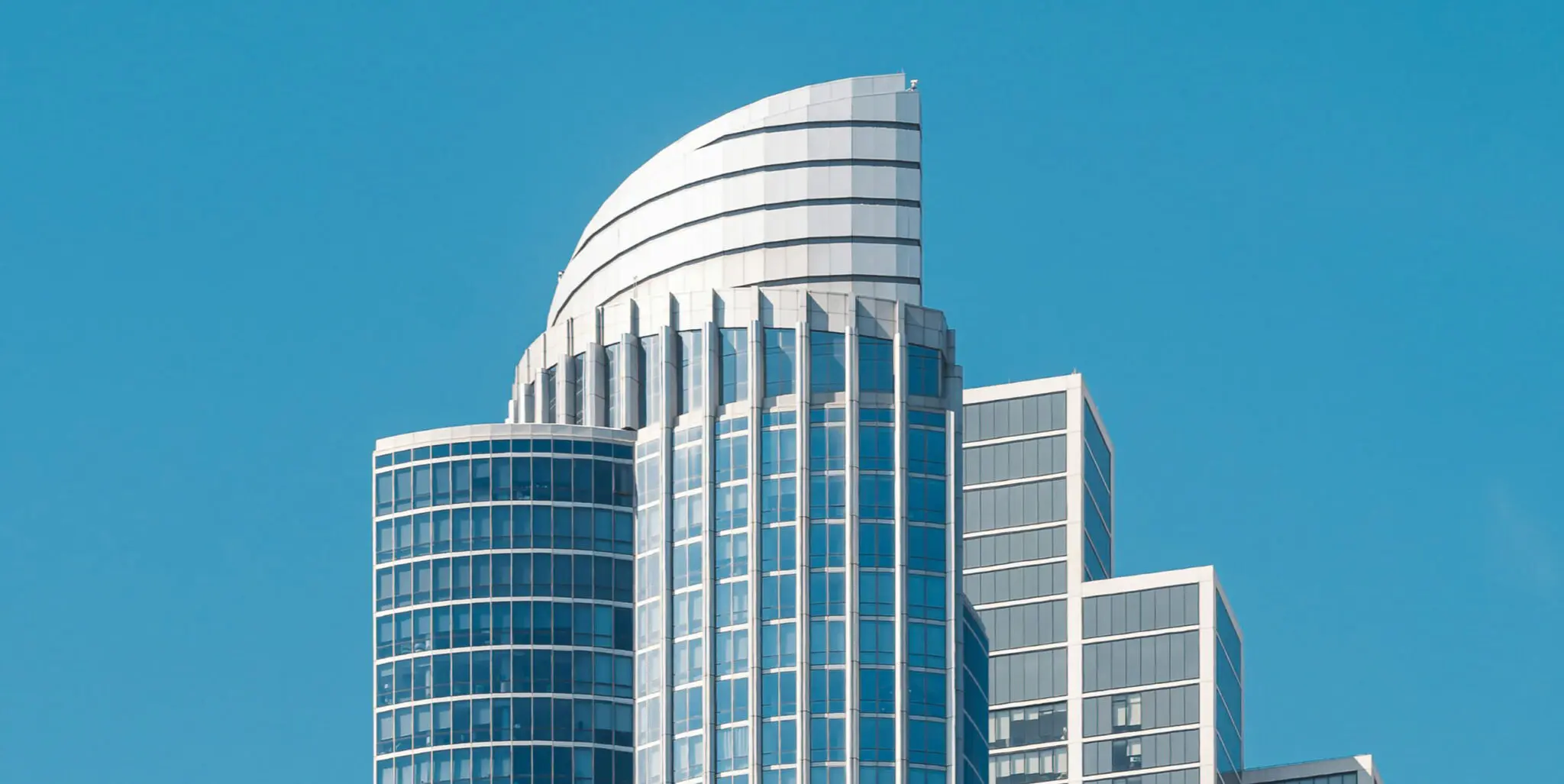 A modern high-rise by TN Capital Investments in Naples, FL, features a curved glass façade and sustainable design against blue sky.