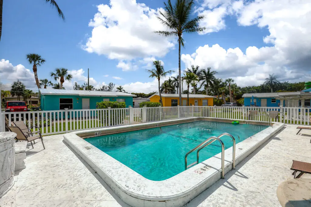 Relax by the outdoor pool with a metal ladder, offered by TN Capital Investments in Naples, FL; lush grounds and palm trees.