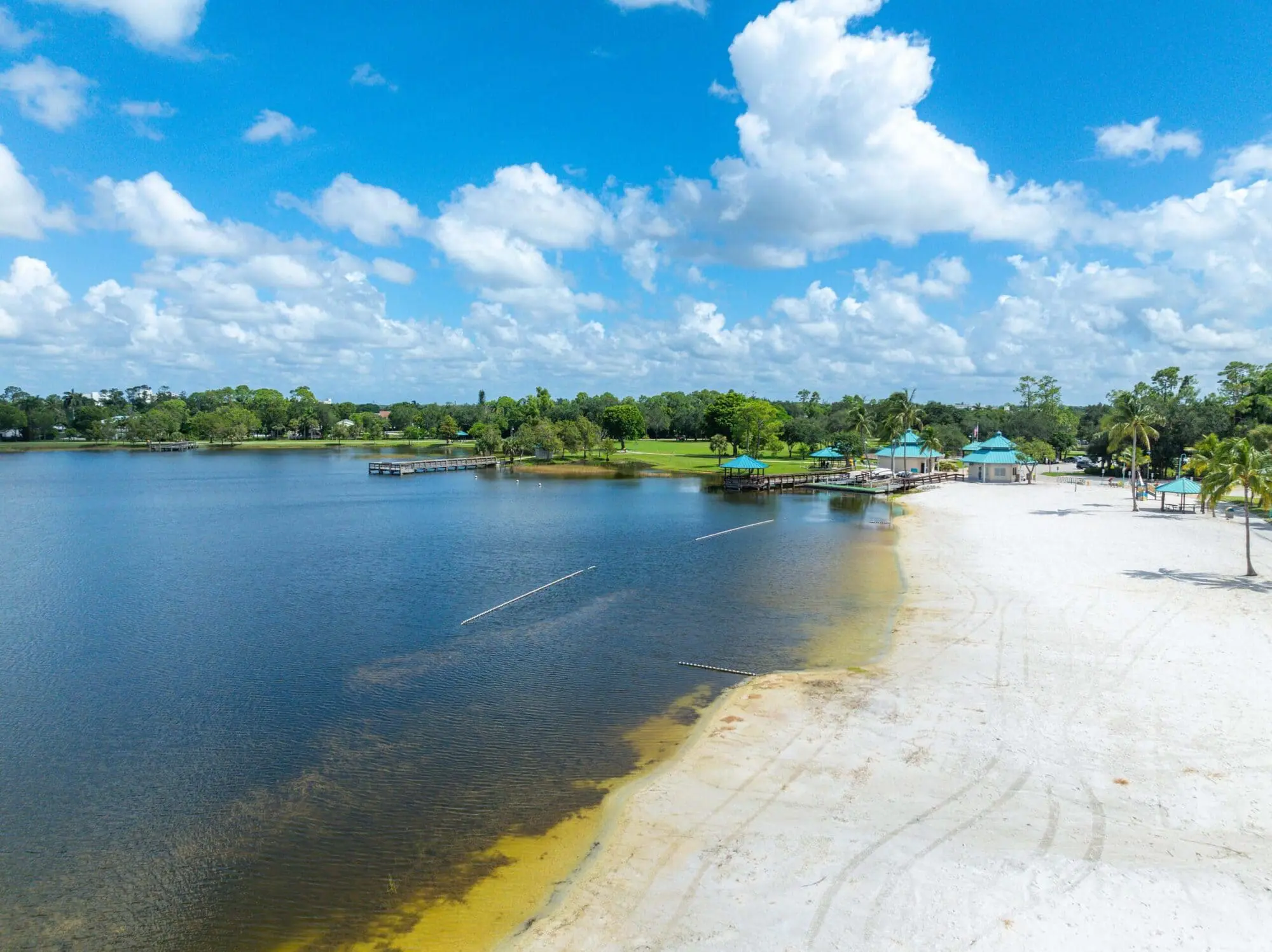 A sandy beach and calm lake with piers and pavilions, near green trees and grass, features TN Capital Investments in Naples, FL.