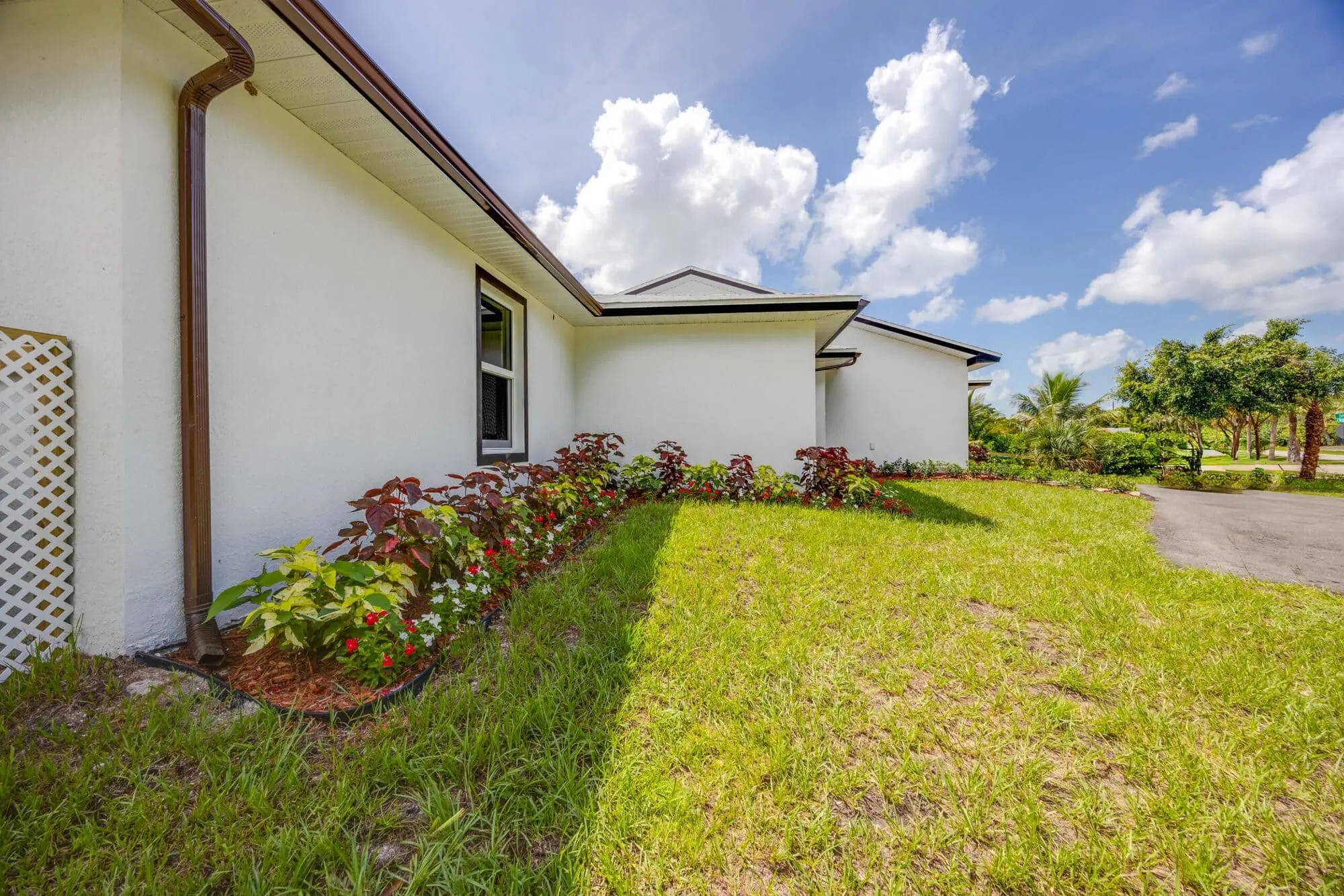 A white house with brown gutter, flower bed, lawn, and driveway under partly cloudy sky—TN Capital Investments in Naples, FL.
