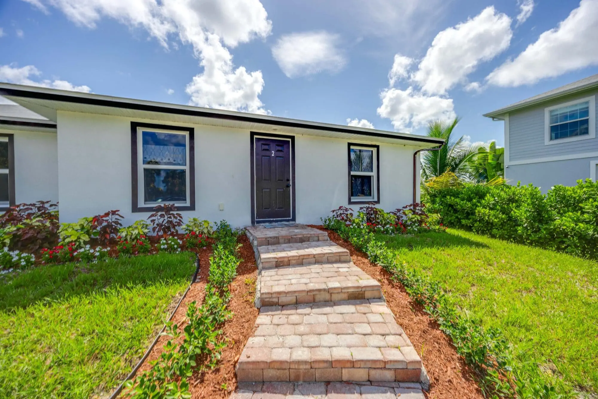 A single-story white house with a dark door and landscaped garden, offered by TN Capital Investments in Naples, FL.