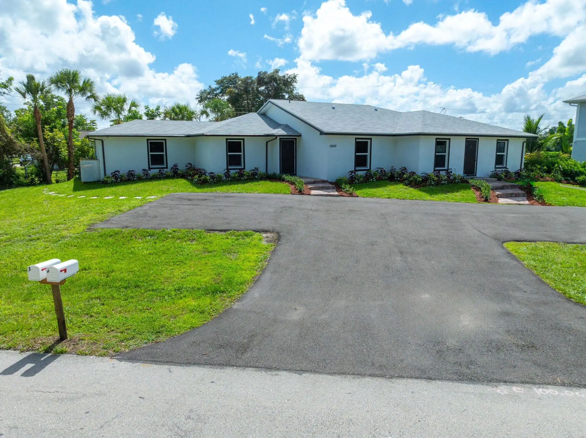 In Naples, FL, TN Capital Investments offers a single-story duplex with gray roof, white exterior, wide drive, and grassy lawn.