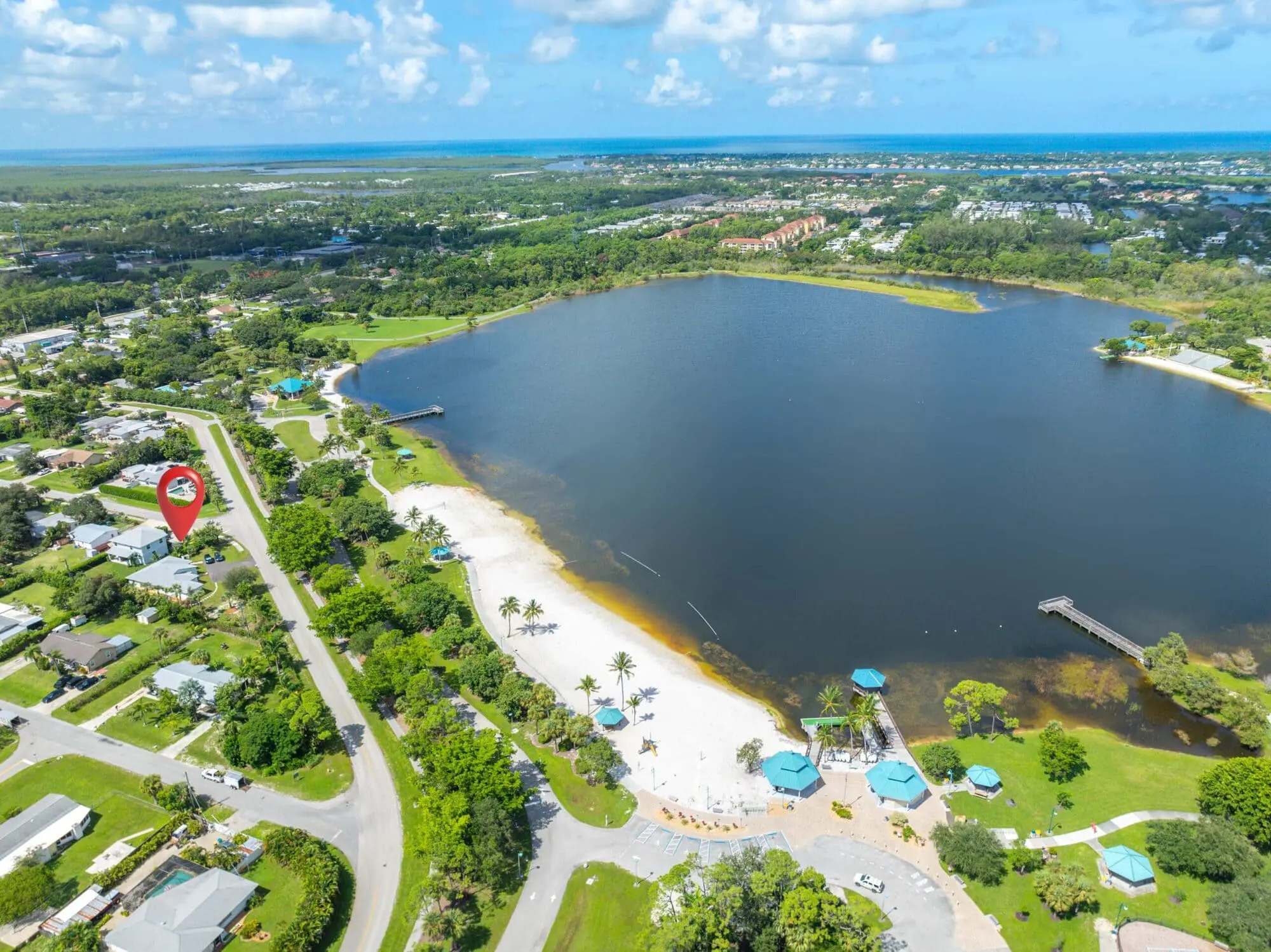Aerial view of TN Capital Investments park in Naples, FL with sandy beach, picnic shelters, dock, and homes under a cloudy sky.