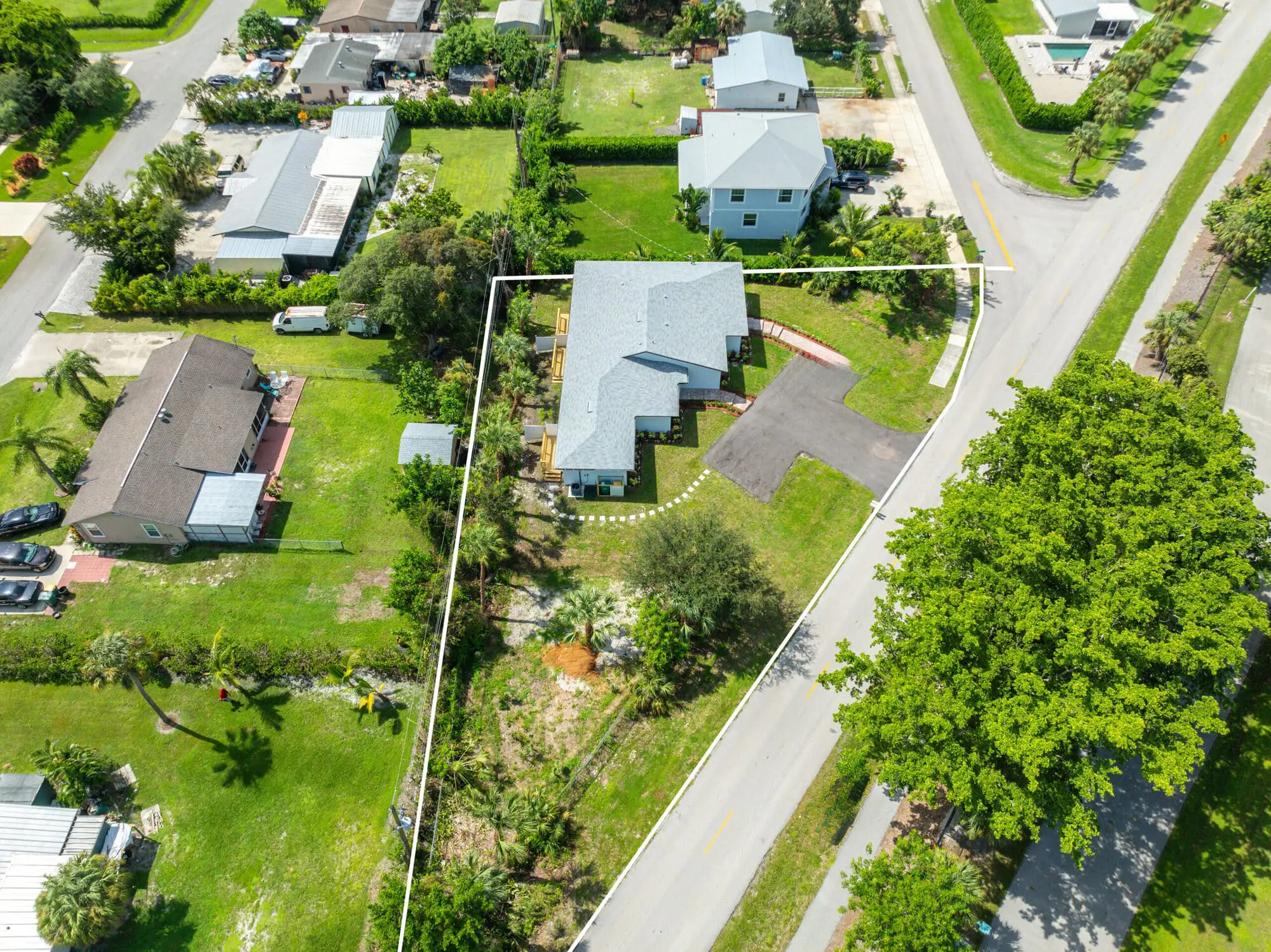 Aerial view in Naples, FL shows a TN Capital Investments single-family home on a white-outlined triangular lot with driveway and trees.