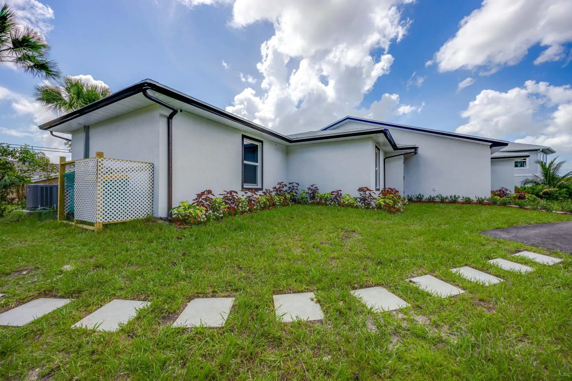 A white single-story house with a sloped roof and garden, for TN Capital Investments in Naples, FL, under a partly cloudy sky.