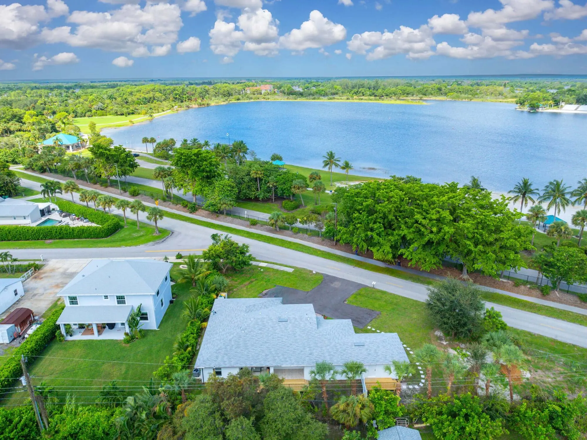 Houses by a curved road with a large lake and trees, partly cloudy sky; TN Capital Investments in Naples, FL.