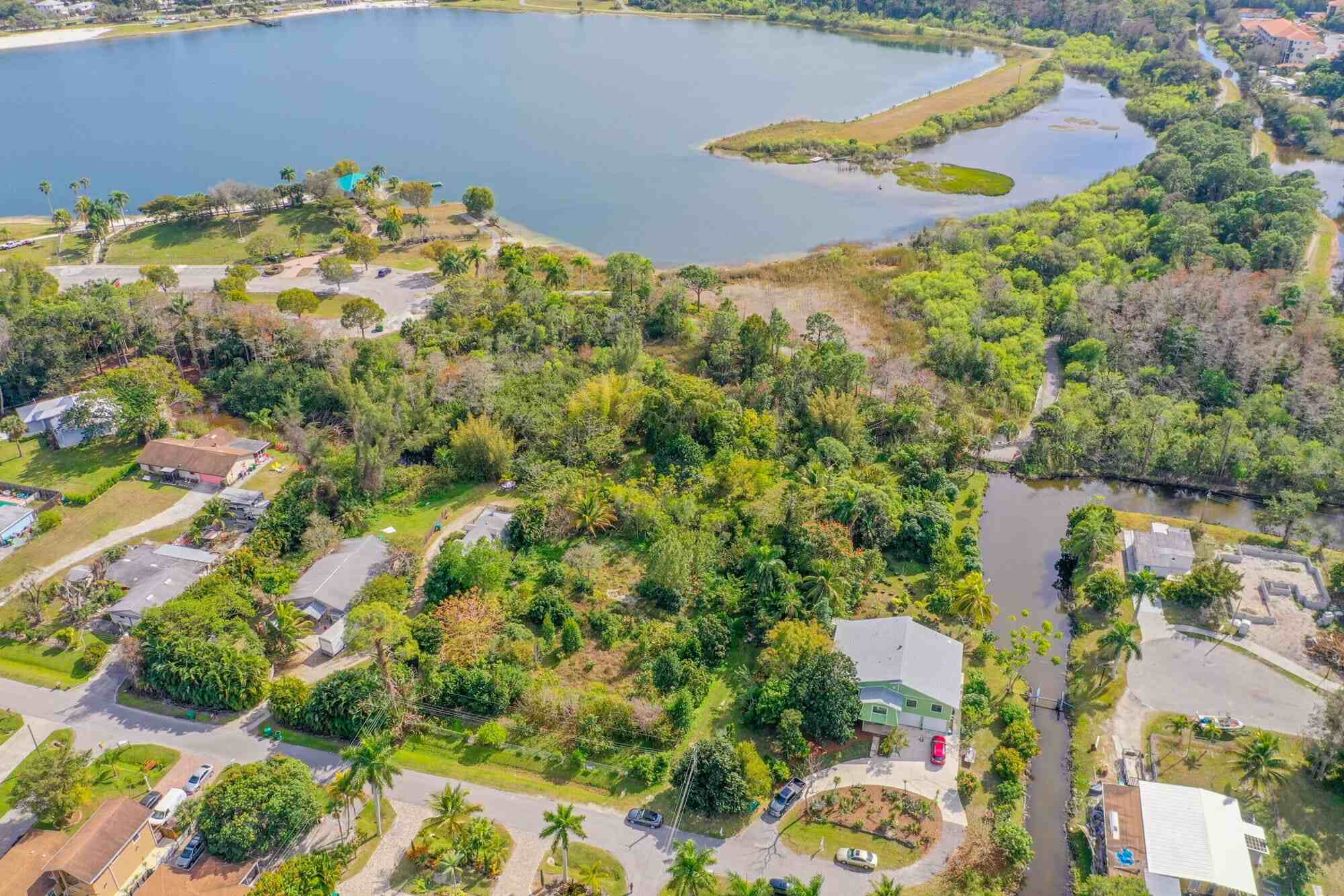 Aerial view of TN Capital Investments properties in Naples, FL, shows houses, trees, and a canal by a lake with greenery and woods.